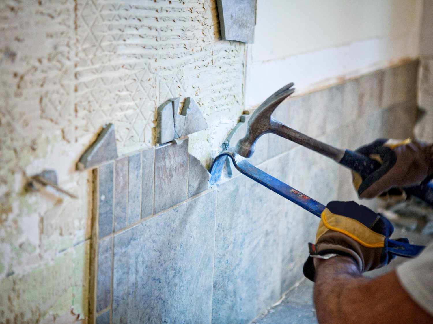 Removing damaged stone wall tiles with a hammer and pry bar before repair